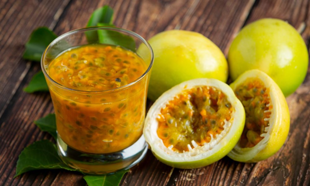 a glass of passion fruit juice and fresh passion fruit cut in half place on wooden  floor